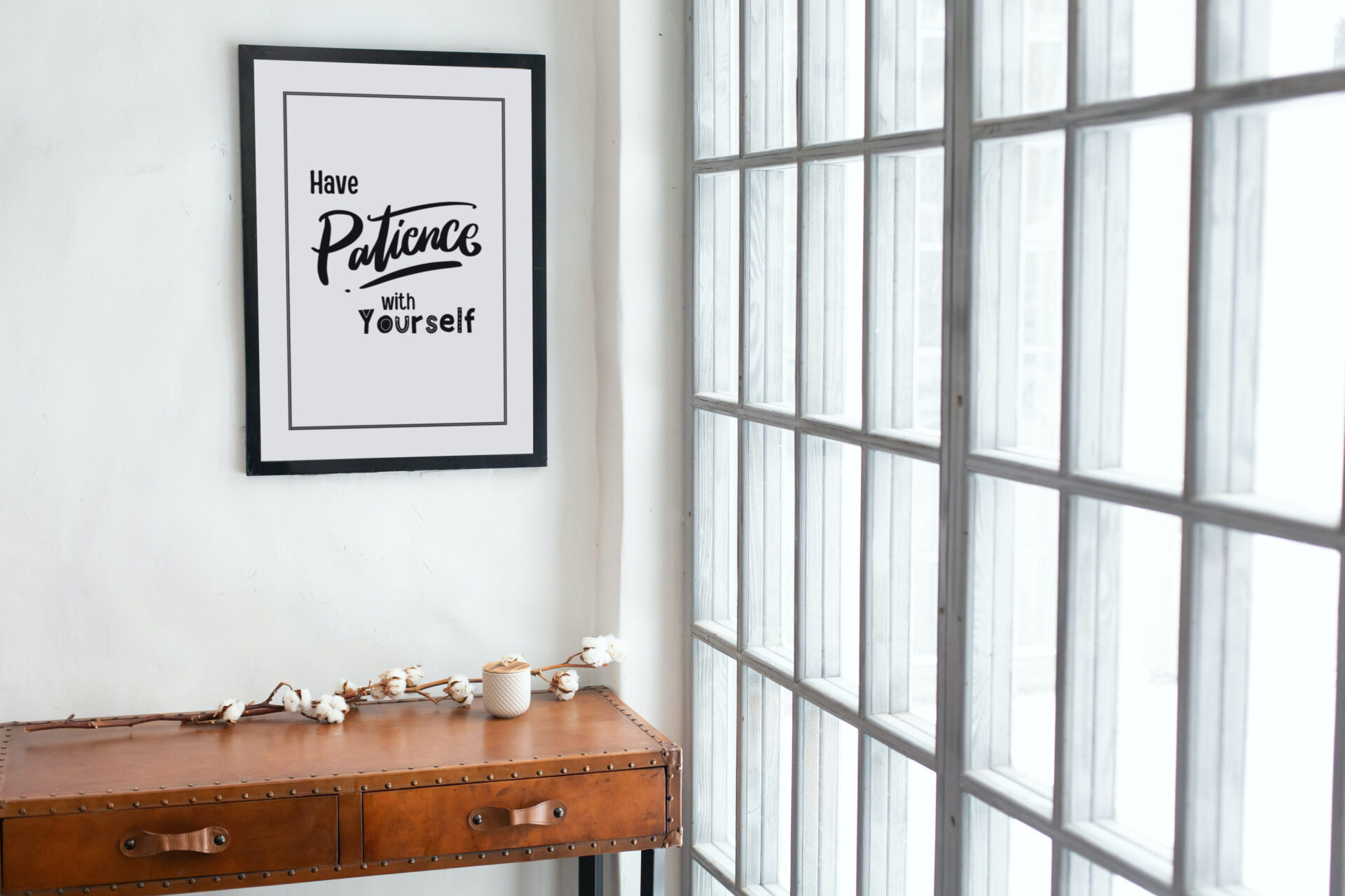 Black wooden portrait frame hanging over the wooden table in the hallway near the window Have Patience